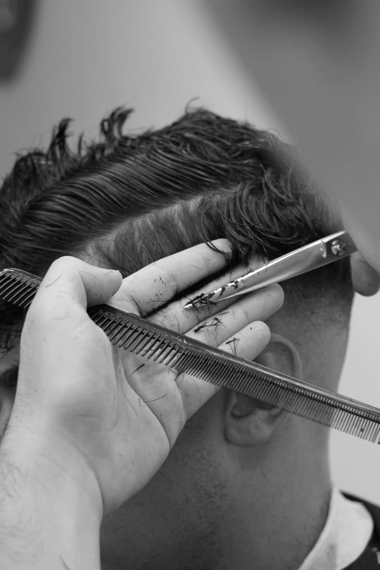 Schere und Kamm schneiden das Deckhaar an der Seite eines Herrenkopfs, Schwarzweissaufnahme